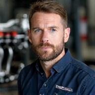 Porträt eines hochqualifizierten Mechanikers in Arbeitskleidung, mit einer fokussierten, kompetenten Haltung in einer luxuriösen Autowerkstatt.